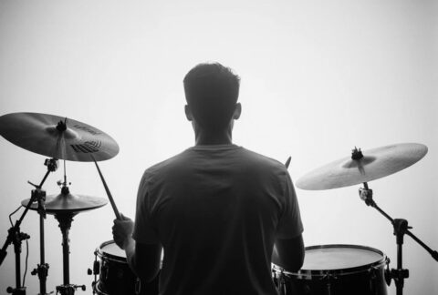 Une photo apaisante d’un batteur de dos, assis derrière son kit, lumière douce